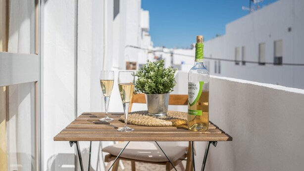 Un balcon avec une table, deux verres de vin blanc, une bouteille de vin et une petite plante en pot.