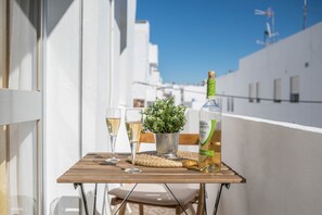 Een balkon met een tafel, twee glazen witte wijn, een fles wijn en een kleine potplant.