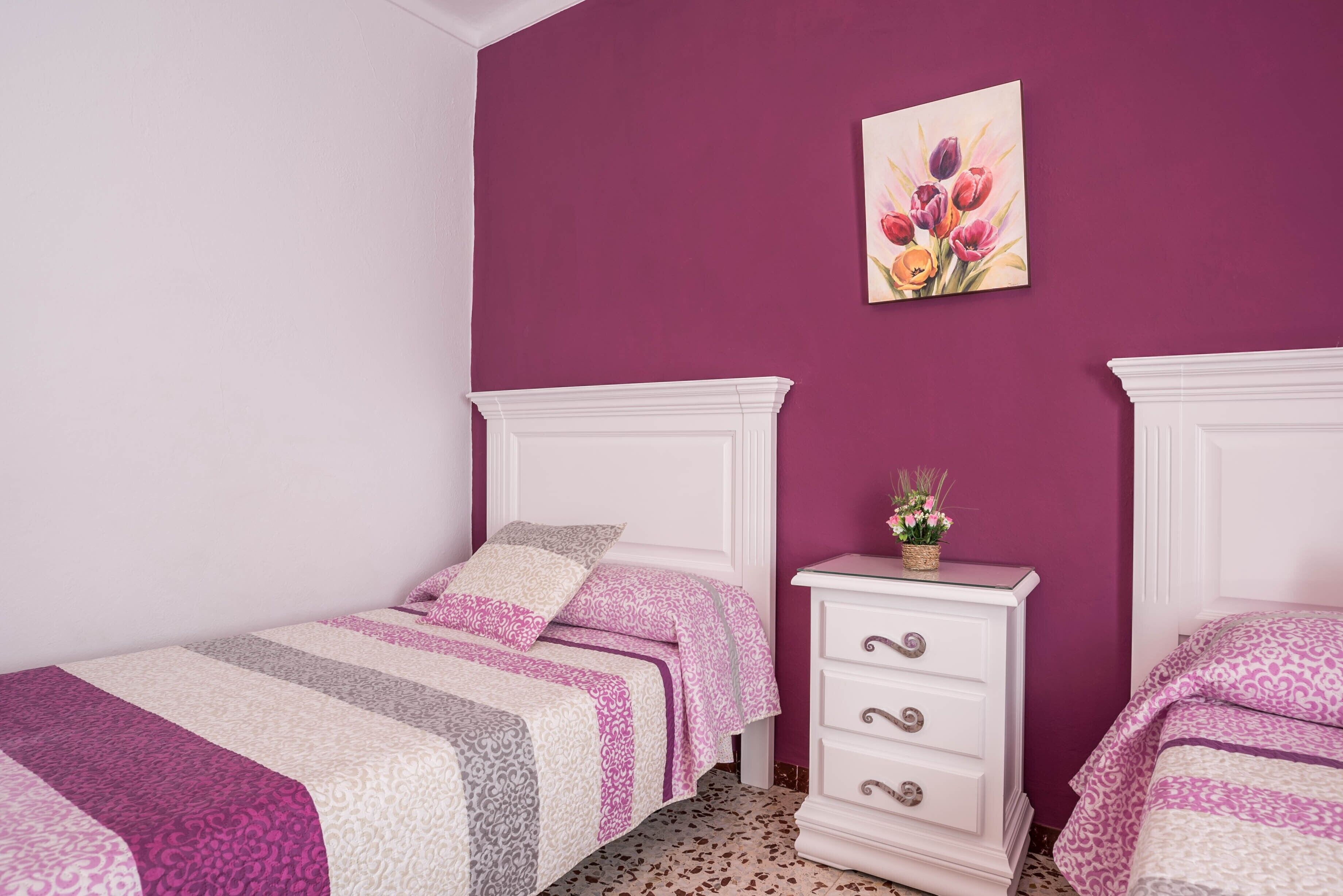 Une chambre avec deux lits, une commode et un tableau mural.