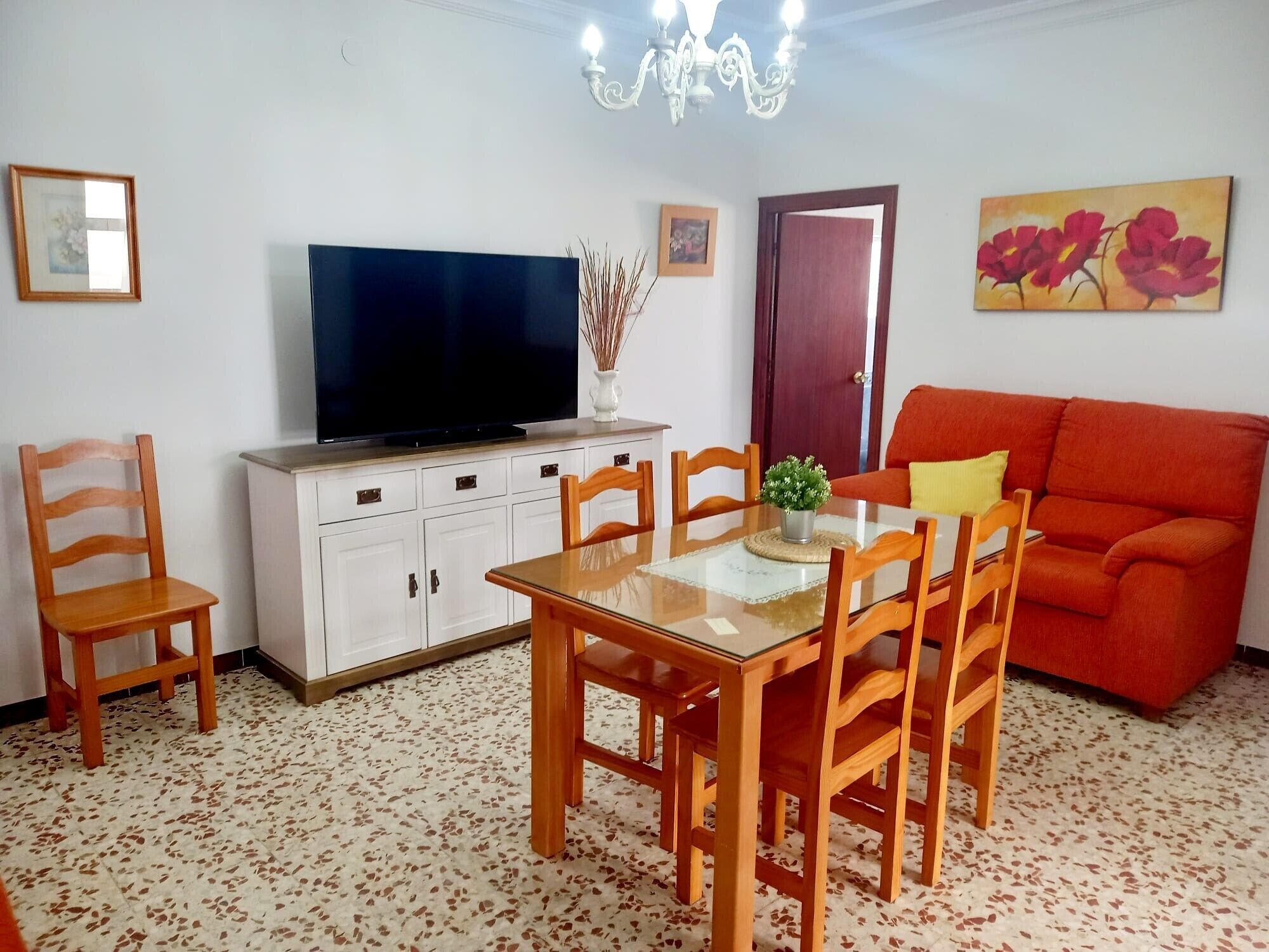Een woonkamer met een televisie, eettafel, stoelen, een bank en een kroonluchter.