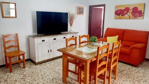 Un salon comprenant un téléviseur, une table à manger, des chaises, un canapé et un lustre.