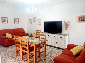 Un salon avec un canapé rouge, une table à manger avec des chaises, un téléviseur à écran plat et un meuble.