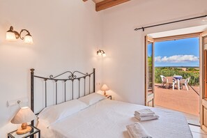 Une chambre à coucher comprenant un lit, des lampes de chevet, une table de nuit et donnant sur une terrasse extérieure avec une table et des chaises.