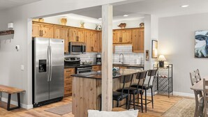 A modern kitchen with wooden cabinets, stainless steel appliances, and a bar area with stools. - Newly Remodeled Townhouse, 2 Master Suites, Hot Tub, SHARC Passes, Bikes (Sunriver)