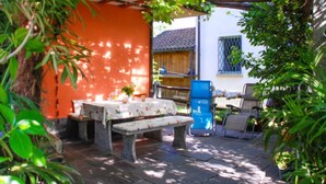 Eine Terrasse mit Tisch und Bank, umgeben von viel Grün und einer roten Mauer.