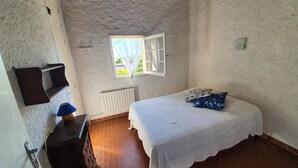 A bedroom with a bed, a window, a radiator, a TV, and a dresser.
