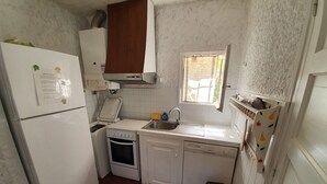 A compact kitchen with white appliances, a window, and a small trash bin.