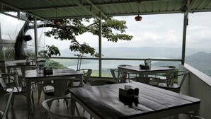 An outdoor dining area with tables and chairs, overlooking a mountainous landscape. - Miraya Hotel (Wai)