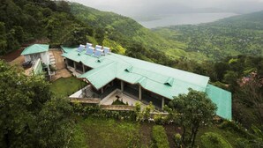 A building with a green roof, surrounded by lush greenery and hills. - Miraya Hotel (Wai)