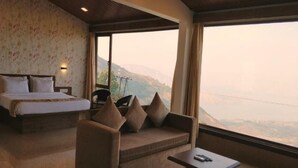 A bedroom with a bed, a sofa, and a table, with a large window offering a mountain view. - Miraya Hotel (Wai)