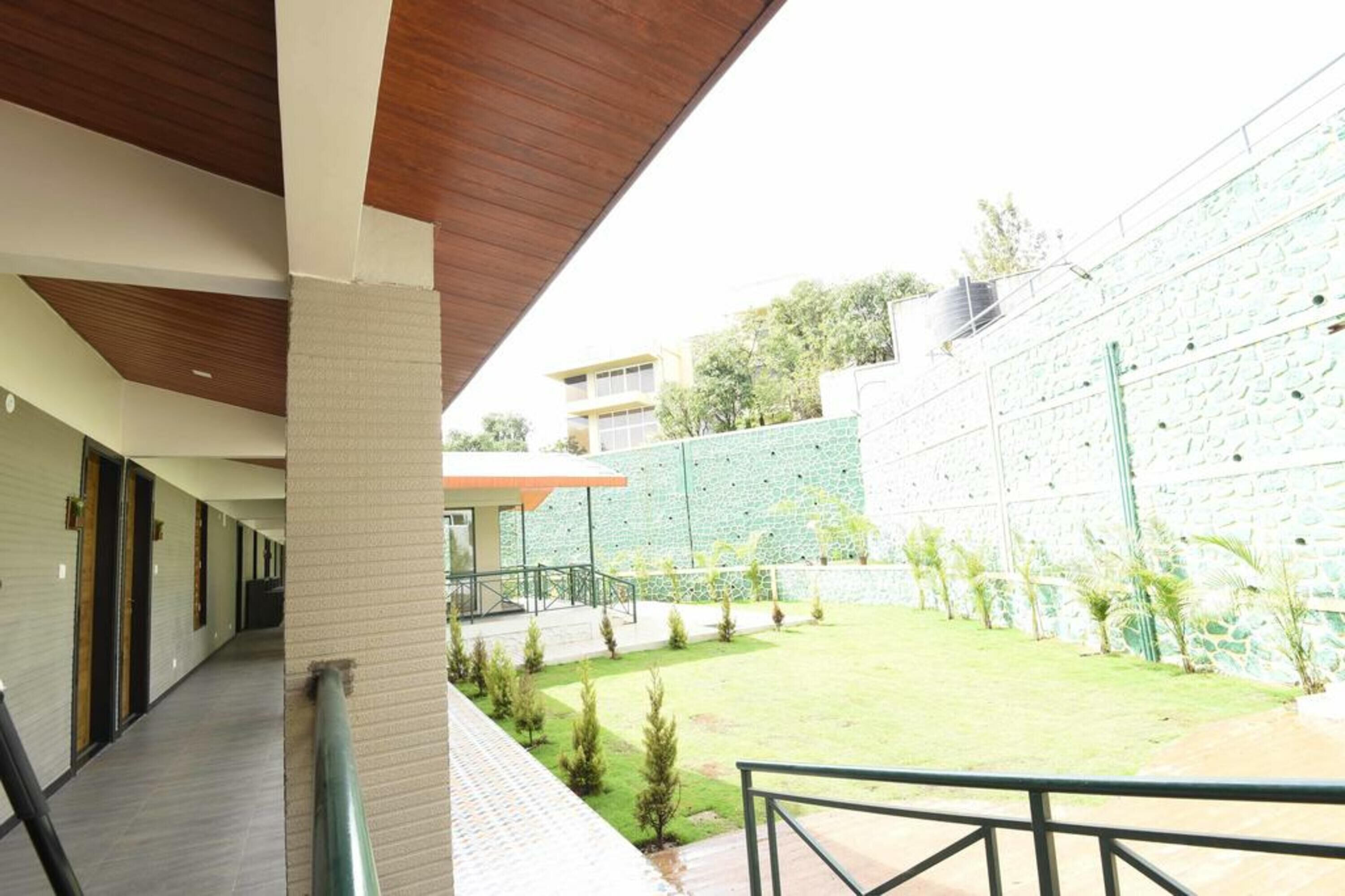 A covered outdoor area with a pathway leading to a building entrance, a small lawn, and a stone wall.