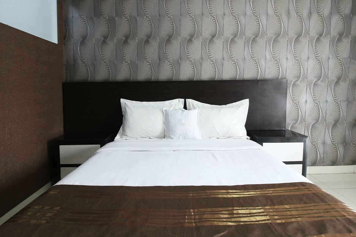 A neatly made bed with white linens and a brown throw blanket.