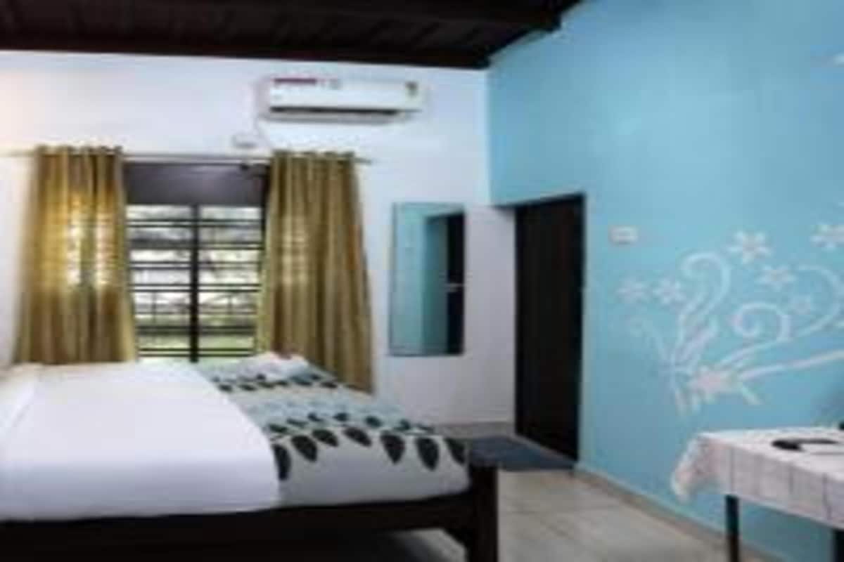 A bedroom with a bed, curtains, an air conditioning unit, and a wall with floral patterns.