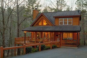 A cabin with a wooden deck, large windows, and a Christmas tree.