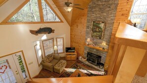 Une pièce de style loft avec une cheminée en pierre, des poutres apparentes en bois, un téléviseur et un canapé.
