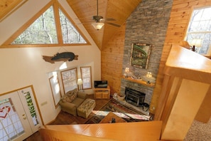 A loft-style room with a stone fireplace, wooden ceiling beams, a television, and a sofa. - Lazy Bear Lair - Minutes from downtown Helen (Helen)
