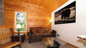 Une pièce chaleureuse avec des murs en bois, un canapé marron, une table basse en verre et un tableau représentant un ours accroché au mur.