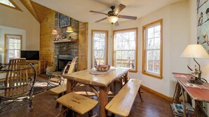 Un intérieur rustique avec une cheminée en pierre, une table à manger en bois, des bancs et un ventilateur de plafond.