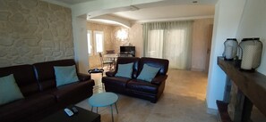 A living room with a stone wall, two leather sofas, a coffee table, and a dining area with a table and chairs.