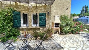Een met stenen bestraat binnenterrein met een tafel, stoelen, een kleine tuin en een gebouw met groene luiken.