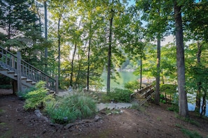 Un escalier en bois mène à une jetée surplombant un lac paisible, entouré d’une végétation luxuriante et d’arbres denses.