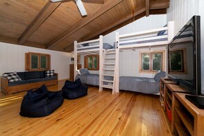 A loft-style bedroom with a bunk bed, a sofa, a TV, and a ceiling fan.