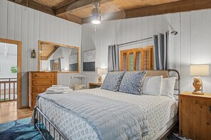 Ein Schlafzimmer mit einem Bett, einem Holzkopfteil, Nachttischen, einem Spiegel und einem Fenster mit Vorhängen.