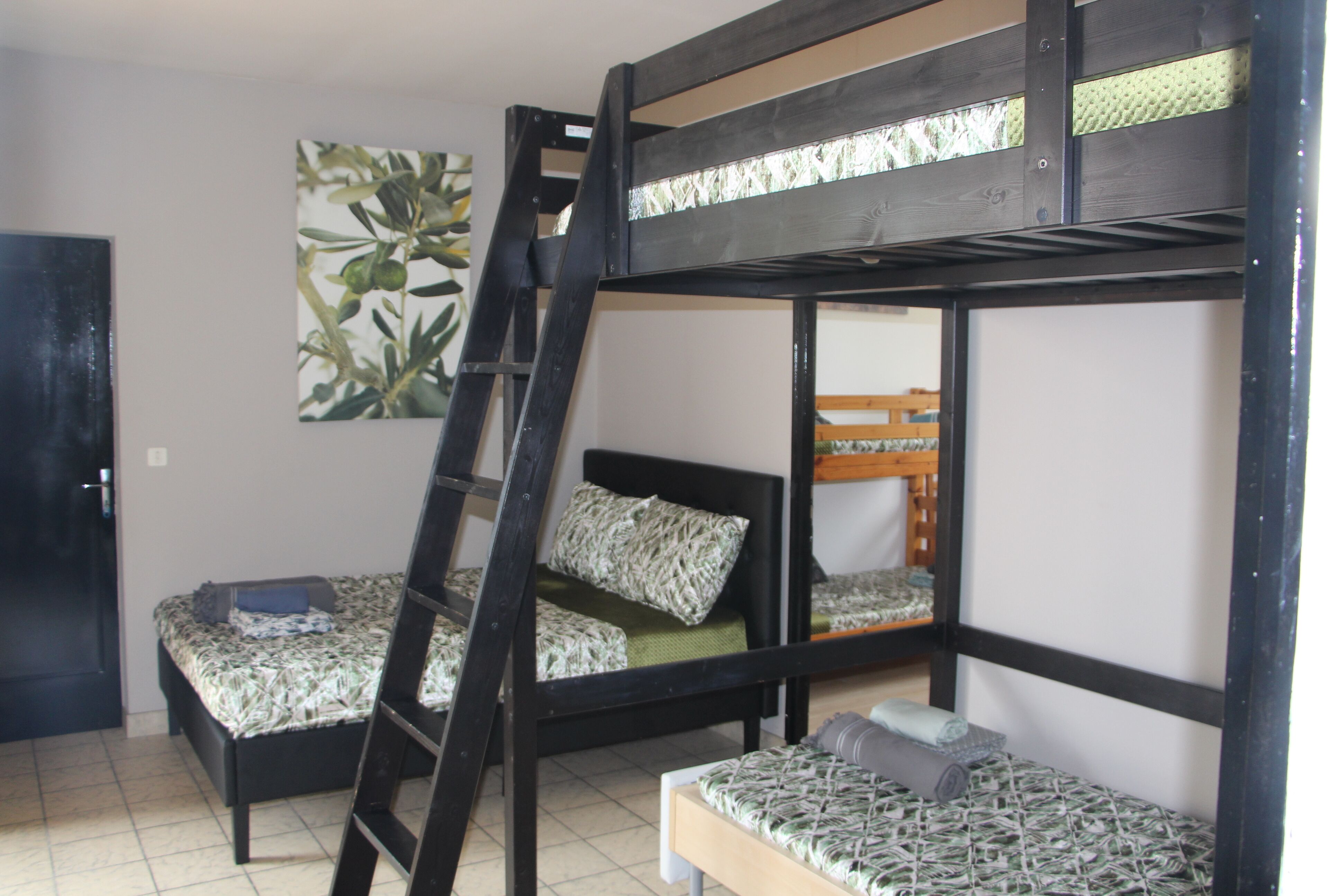 Een slaapkamer met een stapelbed en een ladder, een bed met beddengoed met een patroon, en een schilderij van bladeren aan de muur.