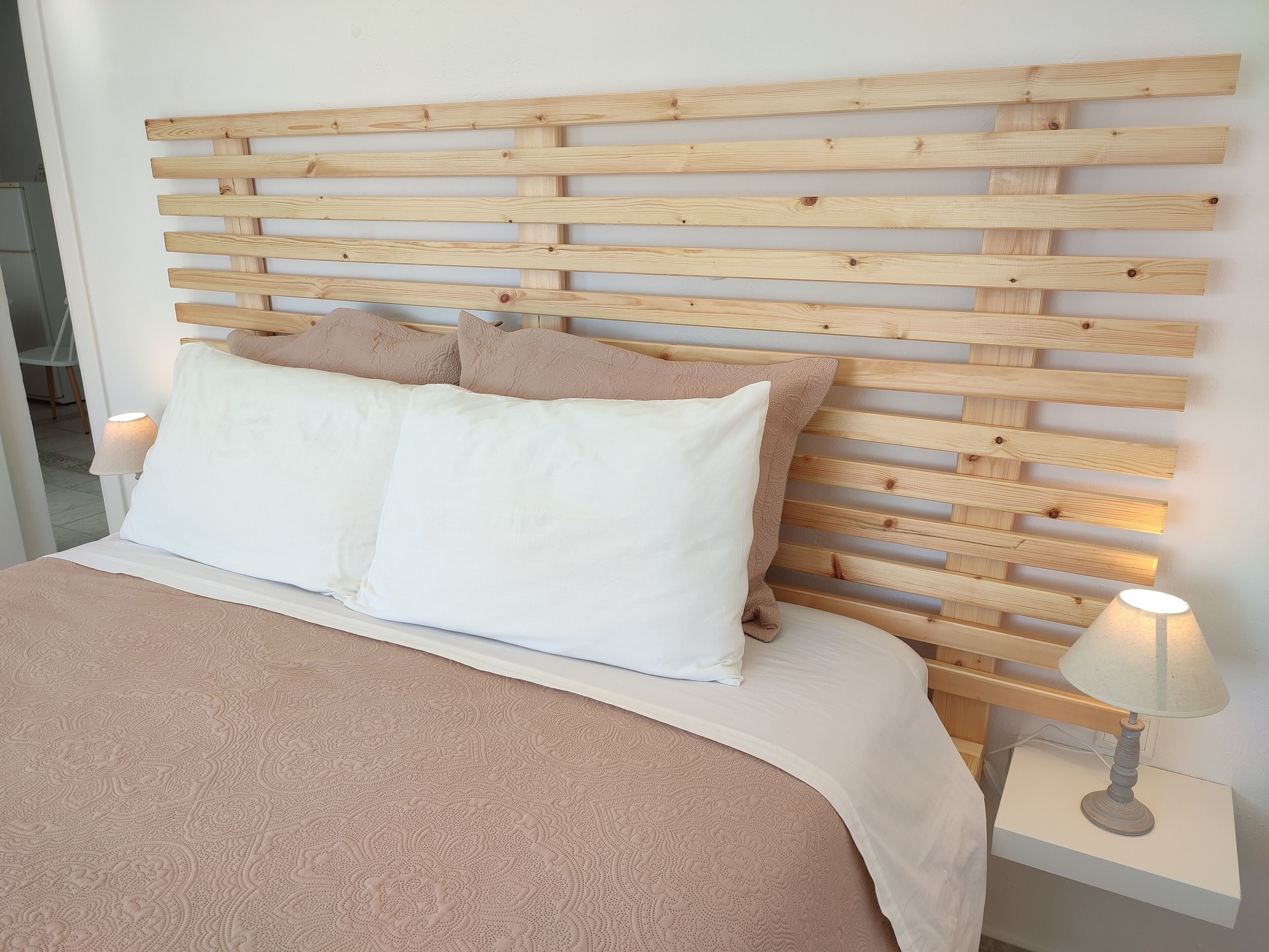 Een bed met een houten hoofdbord, witte beddengoed en een bedlampje.