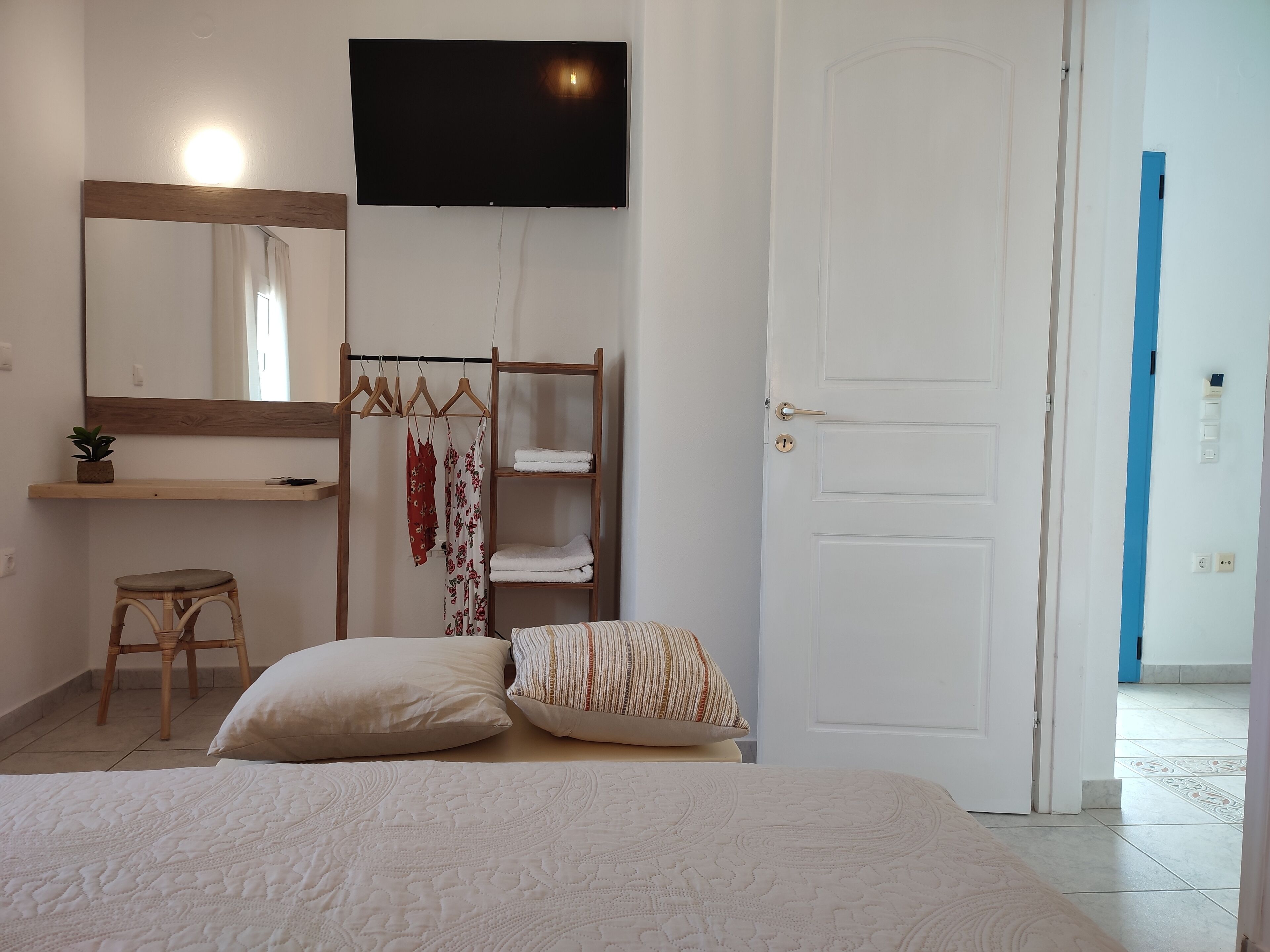 Een slaapkamer met een bed, een houten stoel, een plank met kleding, een televisie en een deur.