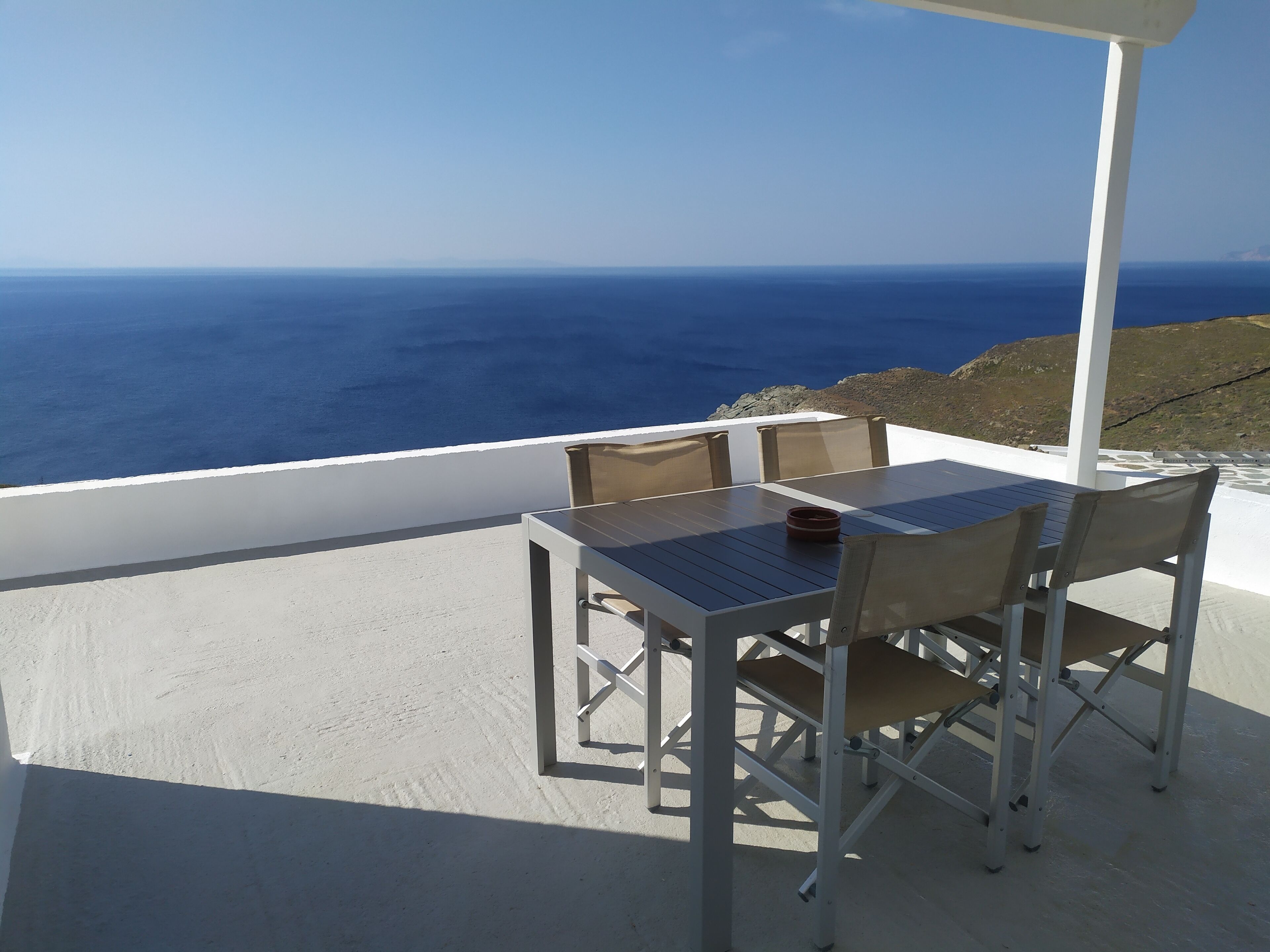 A terrace with a table and chairs overlooking the sea.