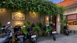 A guesthouse with a signboard, multiple parked motorcycles, and lush greenery. - Cening Ayu Sanur (Denpasar)
