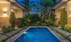 A rectangular pool with a tiled edge, surrounded by various plants and a stone wall. - Cening Ayu Sanur (Denpasar)