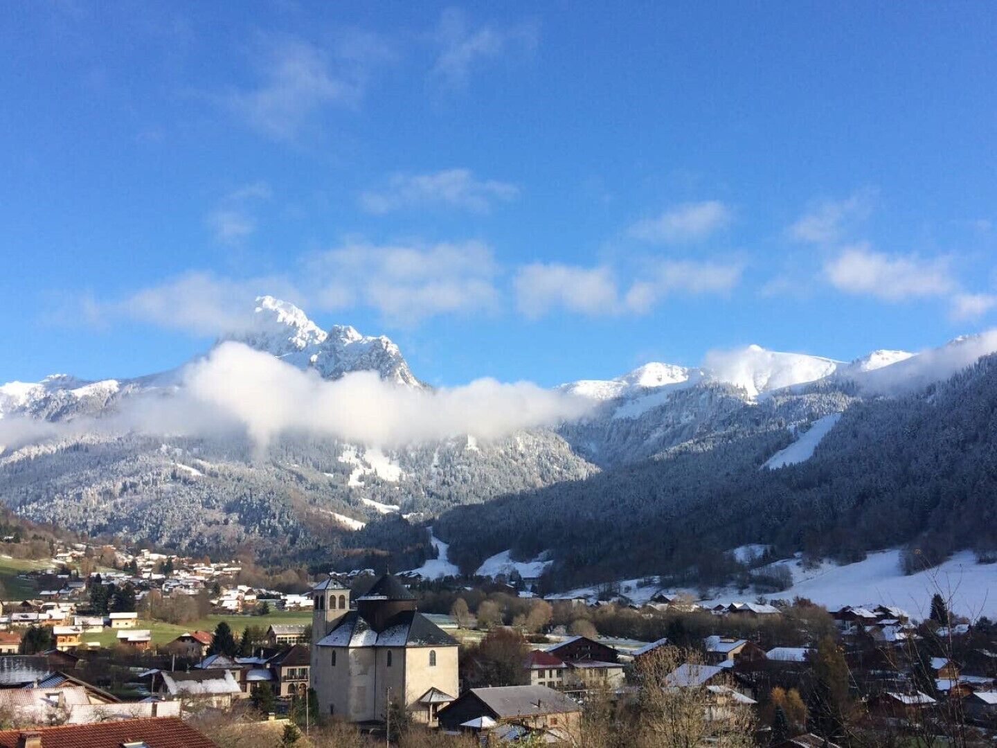A town with a prominent church, snow-covered mountains, and a clear blue sky.