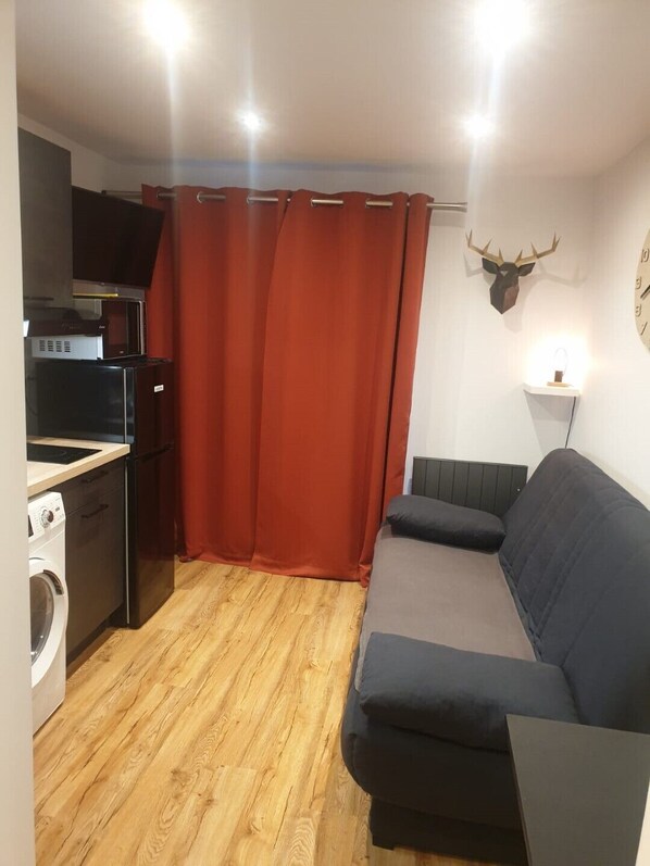 Un espace de vie compact comprenant un coin cuisine, un canapé, un lave-linge et une décoration murale représentant une tête de cerf.