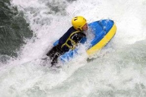 Une personne à bord d’un radeau bleu et jaune navigue dans des rapides aux eaux tumultueuses.