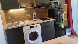 Una cuina compacta amb rentadora, cafetera, nevera i televisió.