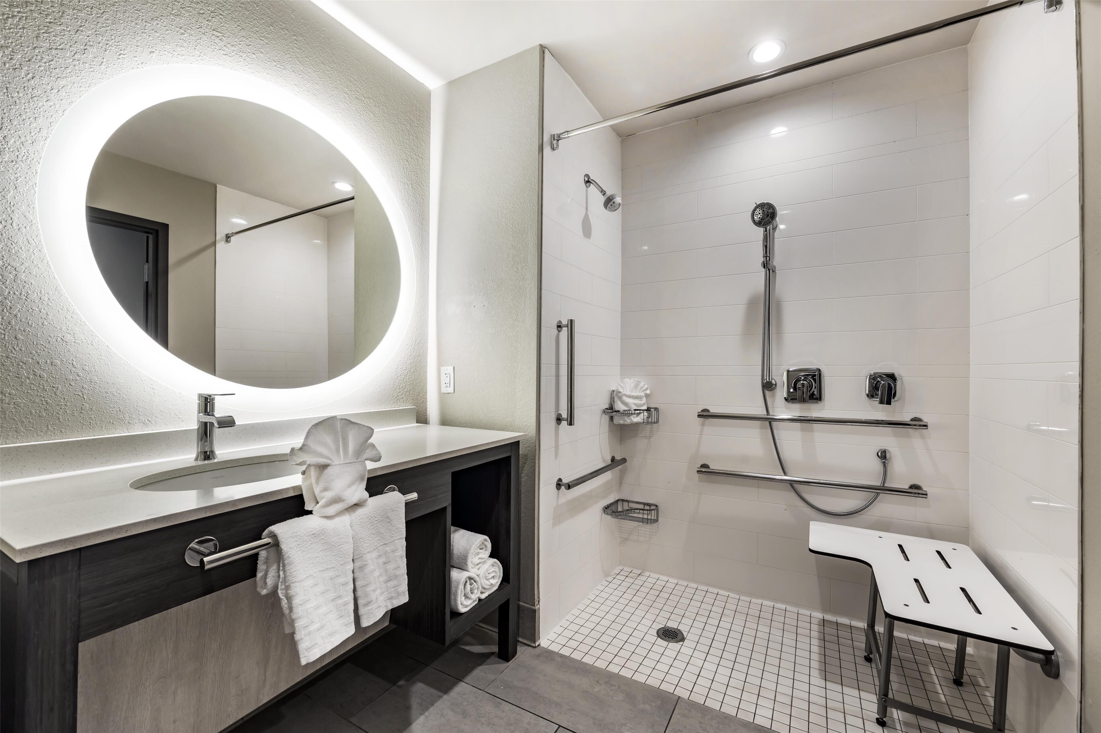 A modern bathroom with a large mirror, a sink, a shower with a glass door, and a small bench.