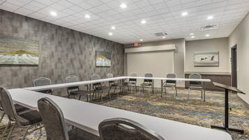 Una sala de conferencias con una larga mesa, sillas, piso alfombrado y una pared gris con dos cuadros enmarcados.