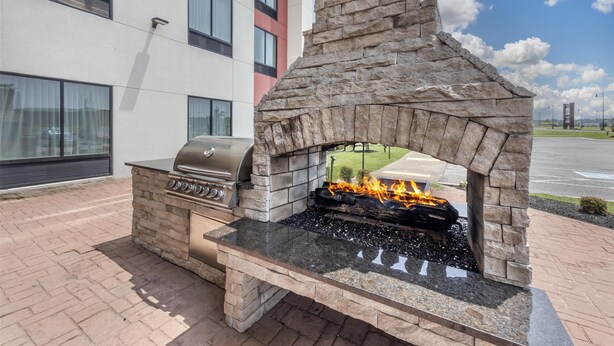 An outdoor stone-built grill with a fire, adjacent to a modern building with large windows. - Best Western Plus Executive Residency Jackson Northeast (Jackson)