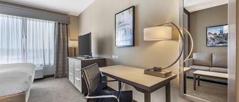 Een hotelkamer met een bed, bureau, stoel, televisie en een grote spiegel.