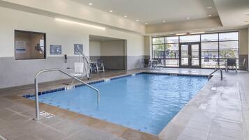A swimming pool with a tiled deck, a safety railing, and a glass door leading to an outdoor area with tables and chairs.