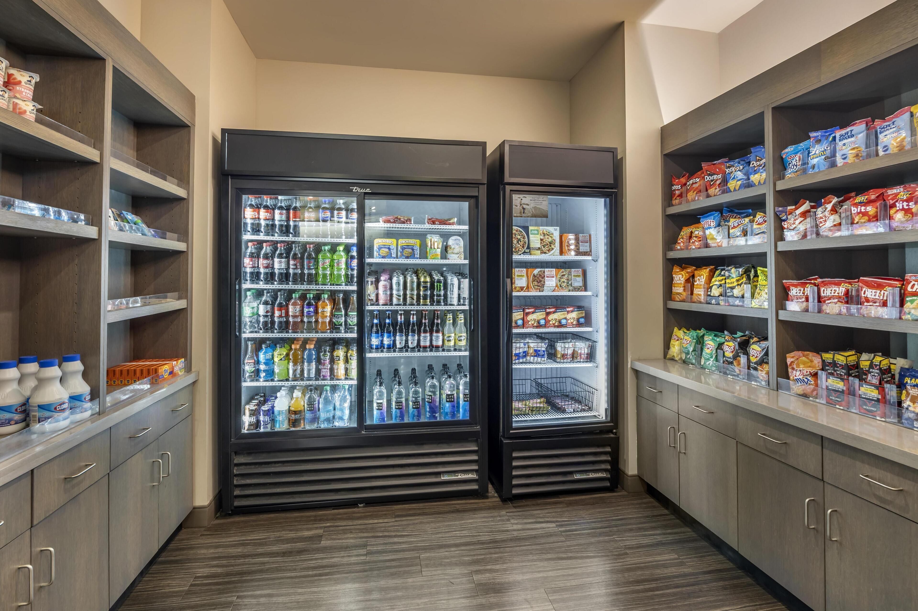 A self-service beverage and snack area with refrigerated drink dispensers and shelves stocked with various snacks and beverages.
