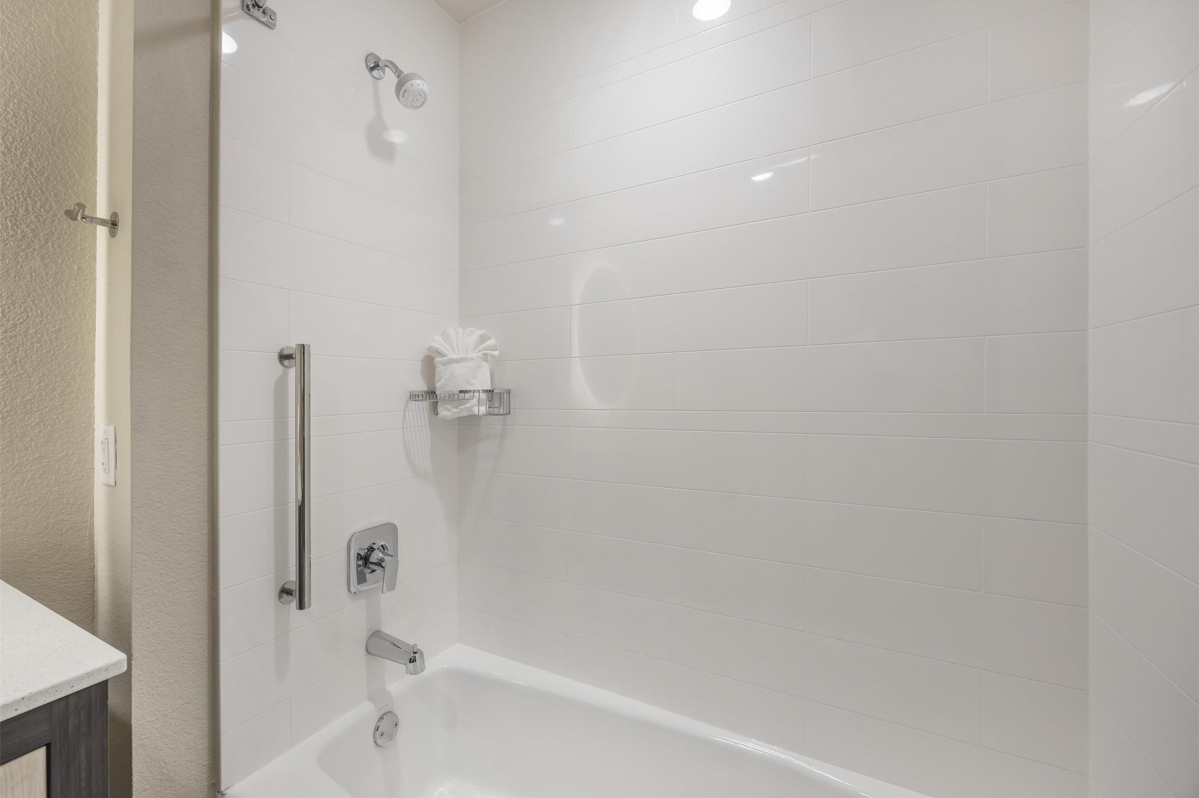 Ein modernes Badezimmer mit weißen Fliesen, einer Badewanne, einer Dusche inklusive Duschbrause und einem Handtuchhalter.