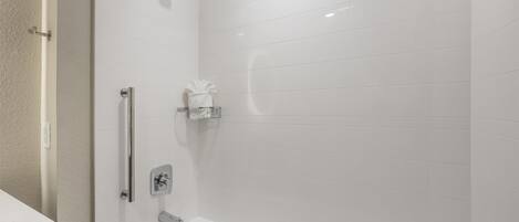 Ein modernes Badezimmer mit weißen Fliesen, einer Badewanne, einer Dusche inklusive Duschbrause und einem Handtuchhalter.