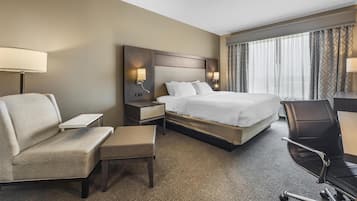 Et hotelværelse med en stor seng, et skrivebord, en stol, en sofa og et natbord med lamper.