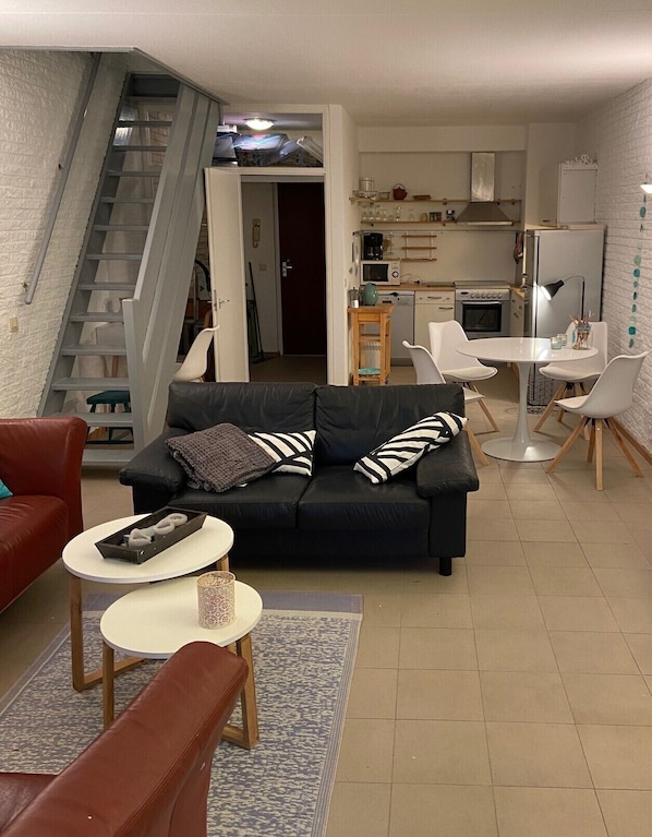 A modern living room with a black sofa, a red armchair, and a small round table with a decorative item. A staircase leads to an upper level.