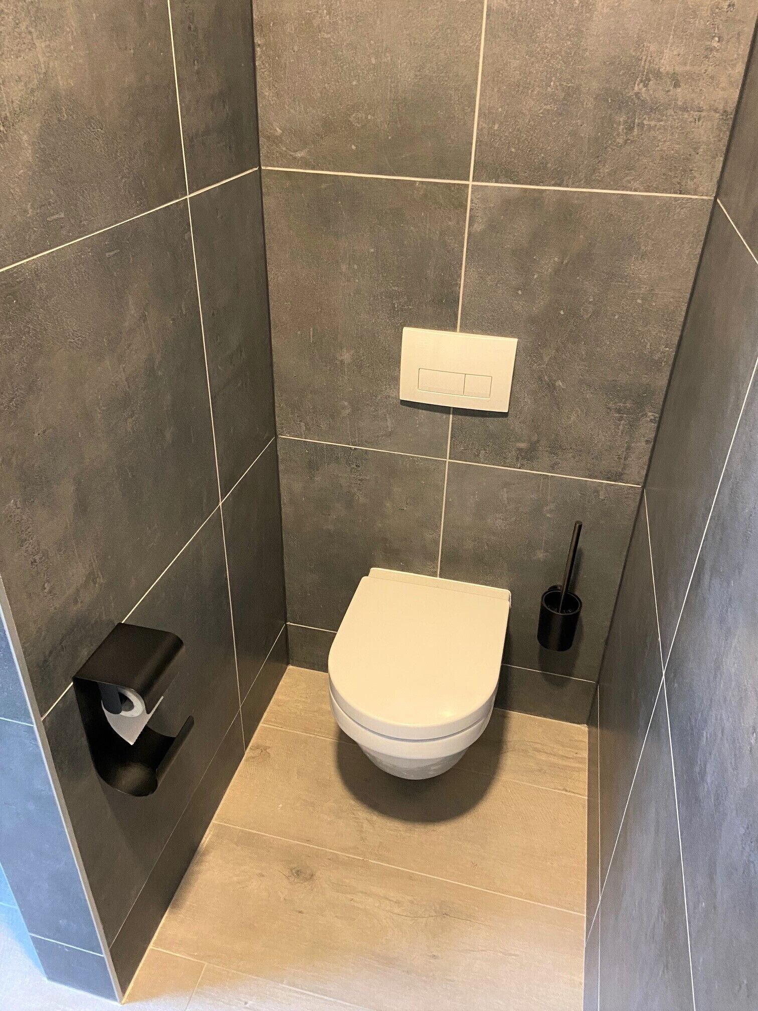 Pieni, moderni kylpyhuone, jossa on wc, käsienkuivaaja ja roskakori.