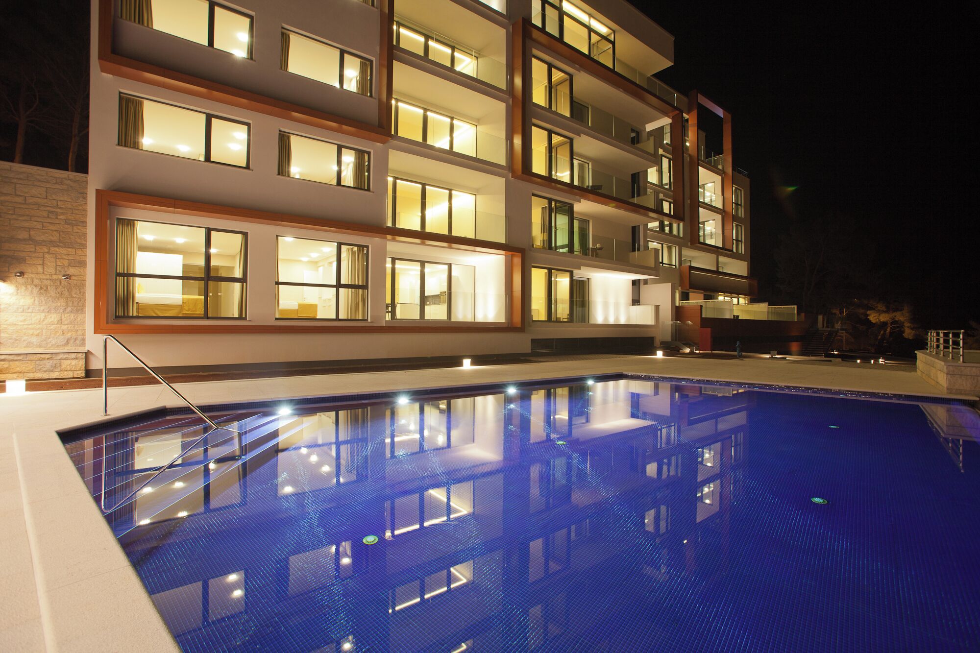 A modern hotel with multiple balconies, a swimming pool, and a stone facade.