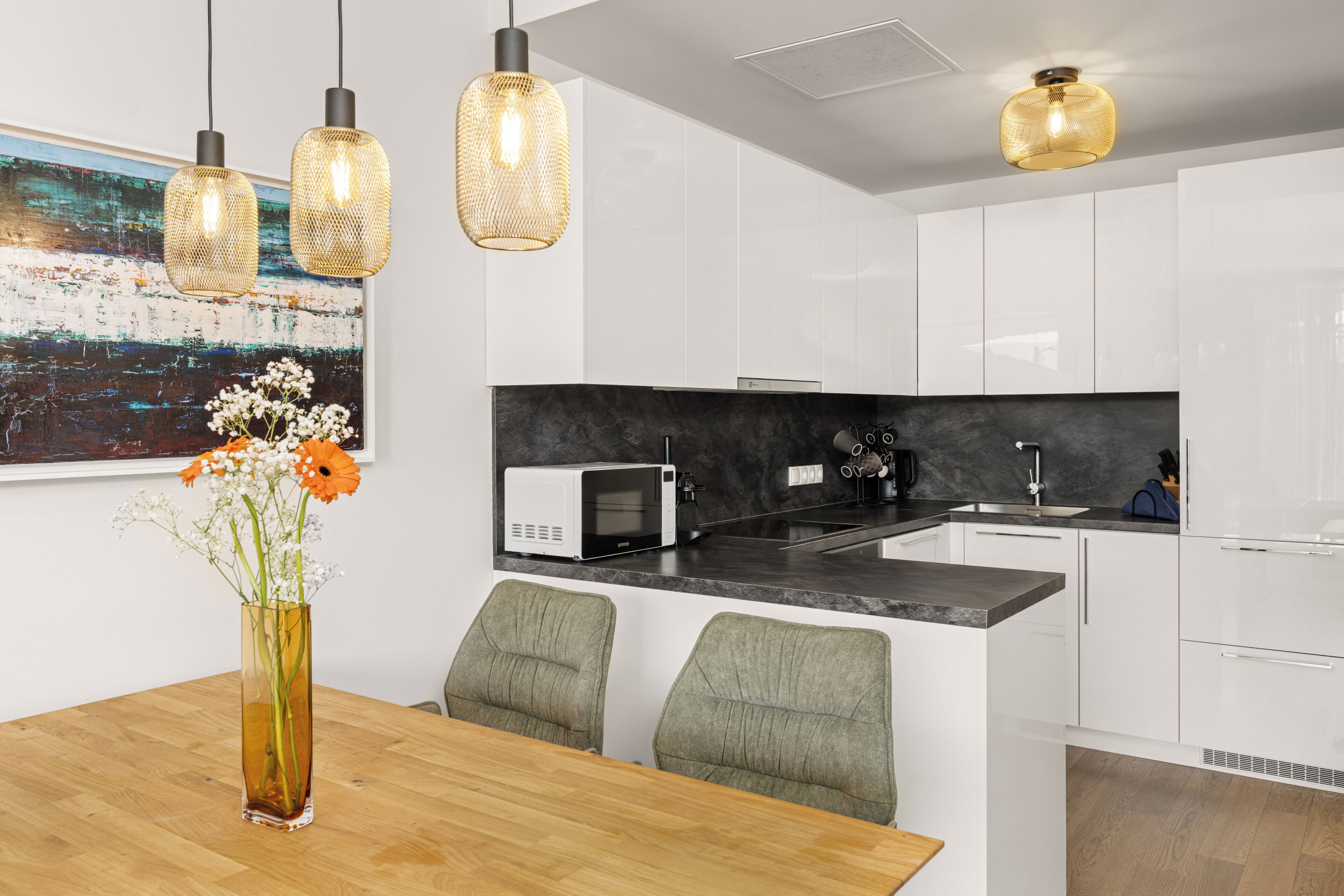 Una cocina moderna con armarios blancos, encimera negra y un comedor con mesa de madera y sillas verdes.